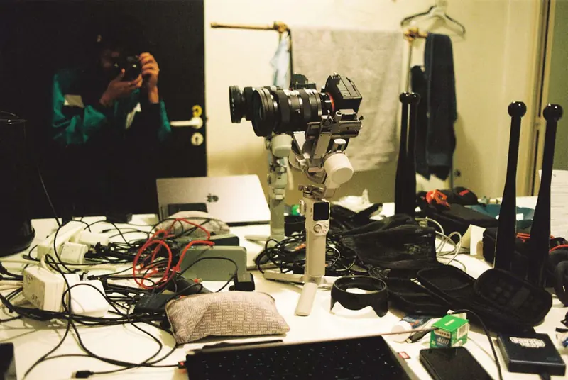 Camera on a gimbal on a cluttered desk, mirror selfie behind. Photo by Iheb Fehri